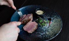 Close-up of a gourmet steak being sliced on a blue ceramic plate with sauce.