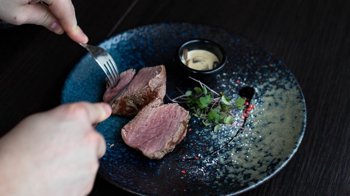 Close-up of a gourmet steak being sliced on a blue ceramic plate with sauce.