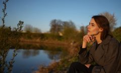 A woman sitting by a lakeside, contemplating nature during sunset.