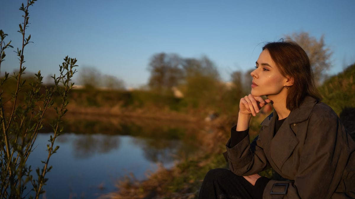 A woman sitting by a lakeside, contemplating nature during sunset.
